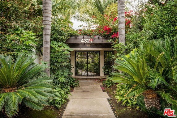 Front view of a house entrance surrounded by lush greenery and palm trees.