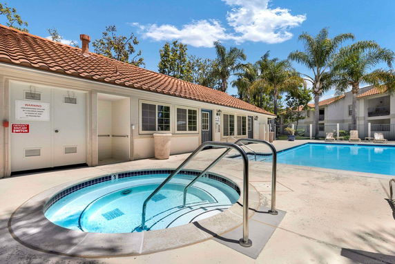 Outdoor pool area with a hot tub adjacent to a building with a tiled roof.