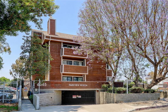 Front view of a multi-story residential building with wooden exterior and parking entrance.