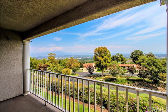 View from a balcony overlooking a scenic landscape with trees and distant hills.