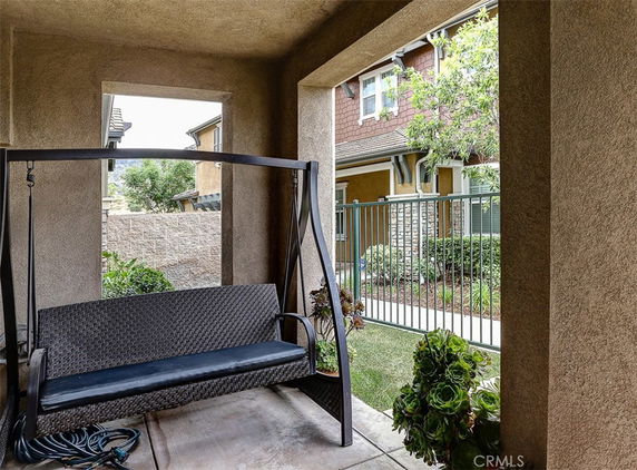 View from a covered outdoor area with a swing seat, looking towards the front of a house with a landscaped yard.