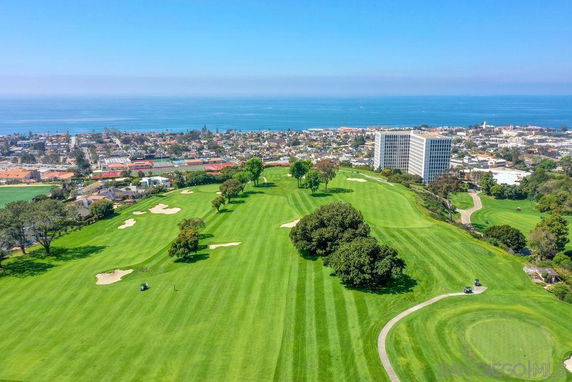 Aerial panoramic view of a golf course with a cityscape and ocean in the background.