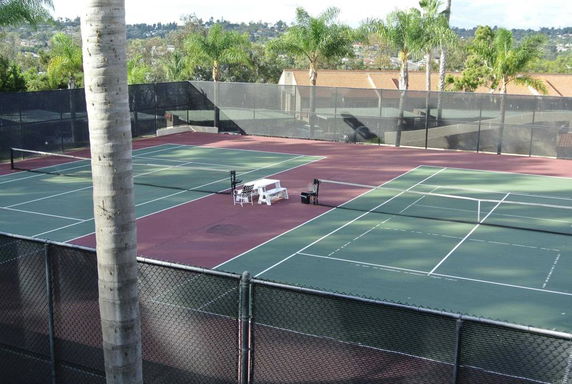 Tennis court with surrounding fence and trees in the background.