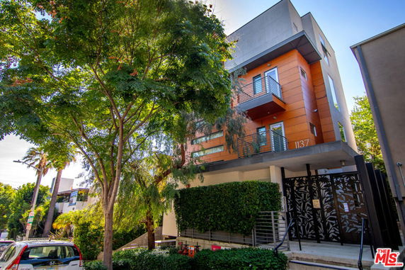 Front view of a modern multi-story building with balconies and a gated entrance.