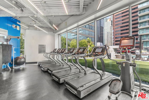 Indoor gym with treadmills and large windows overlooking buildings.