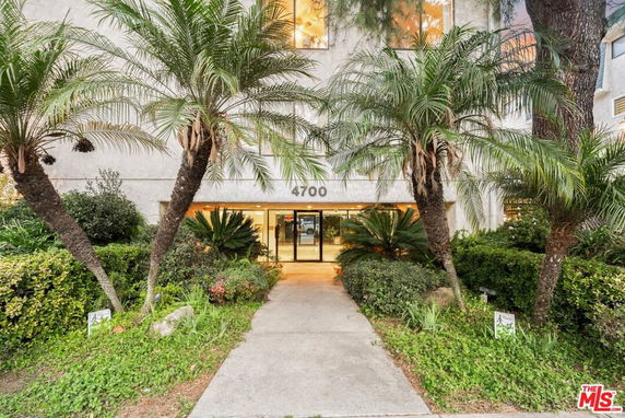 Front view of a building with entrance surrounded by palm trees and greenery.