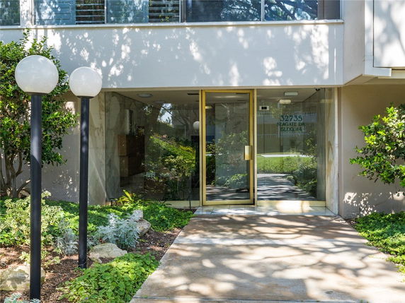 Front view of a building entrance with glass doors and surrounding greenery.
