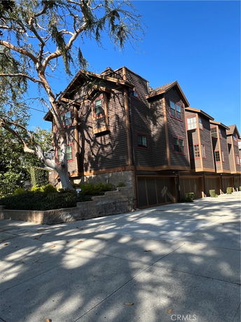 Front view of a multi-story wooden house with multiple windows and a driveway.
