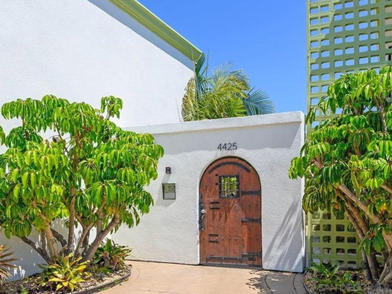 Front view of a building entrance with a wooden arched door set in a white wall.