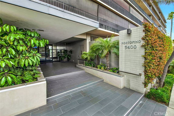 Front view of a modern multi-story building with an entrance walkway and greenery.