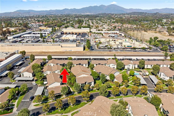 Aerial view of residential community with houses surrounded by trees, roads, and parking areas, with mountains in the background.