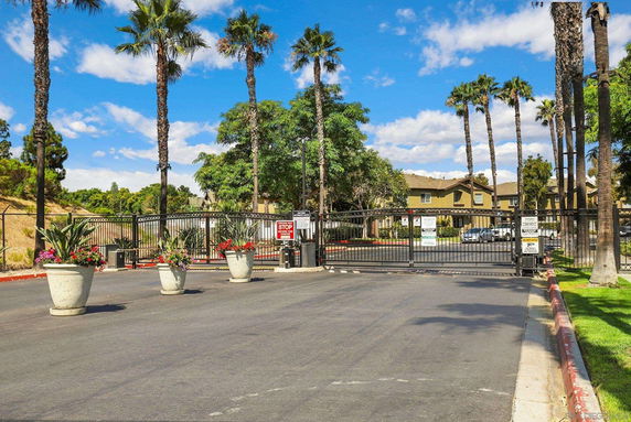 Gated entrance to a housing complex with palm trees and a two-story building in the background.