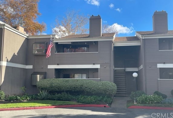 Front view of a multi-story residential building with brown siding and an American flag.