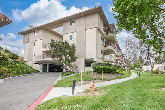 Front view of a multi-story residential building with balconies and a parking area underneath.