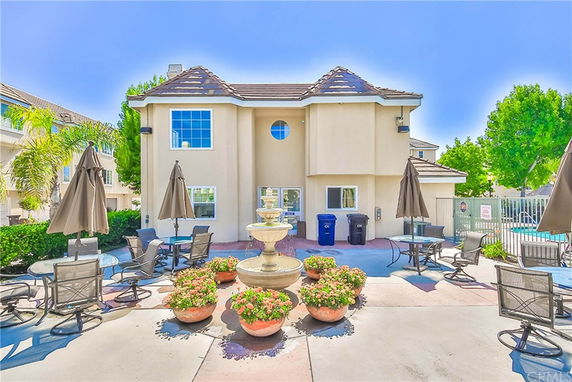 Front view of a two-story house with outdoor seating and a central water fountain.