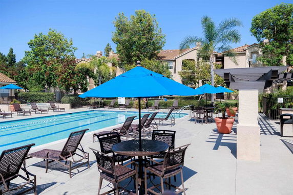 Outdoor swimming pool area with lounge chairs and blue umbrellas.
