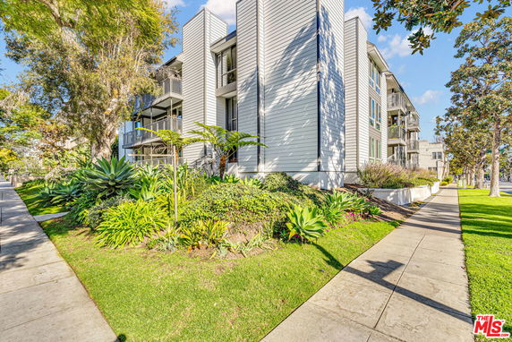 Front view of a multi-story residential building with balconies and landscaped surroundings.