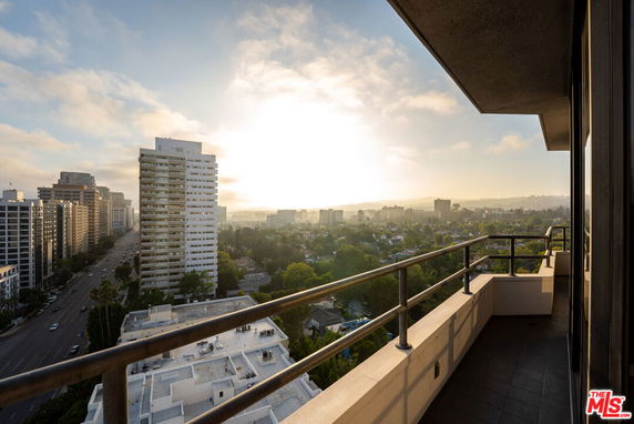 Panoramic view from a balcony overlooking a cityscape with buildings and trees.
