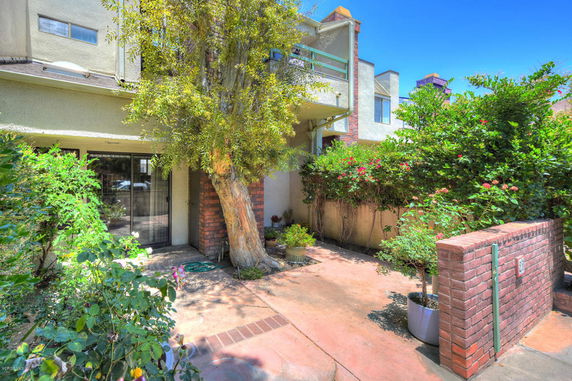 Front view of a multi-story house with brick and stucco elements, surrounded by greenery.