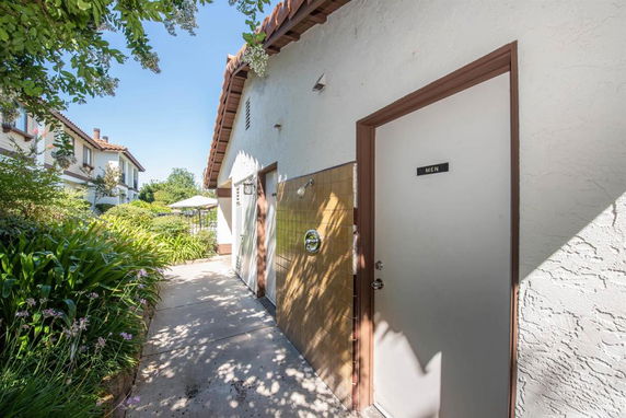 Side view of a building with a tiled roof and a door labeled 'Men'.