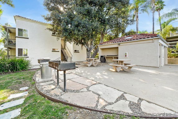 Outdoor area with picnic tables and a barbeque grill next to a building.