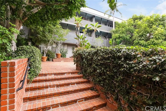 Front view of a multi-story building with brick steps and lush greenery.