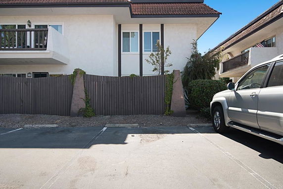 Outdoor parking area next to a building with balconies and a high wooden fence.
