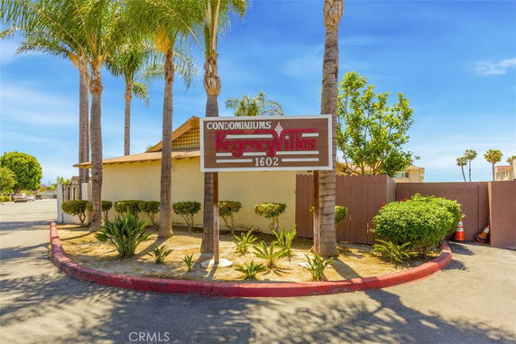 Front view of a condominium building with a sign reading 'Regency Villas 1602' and palm trees in the foreground.