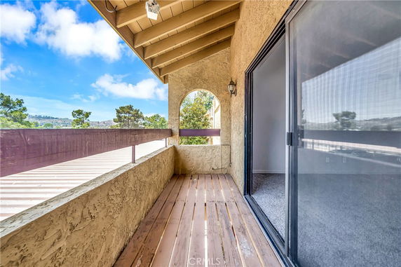 Balcony with wooden flooring and railing, offering a view of distant hills and greenery.