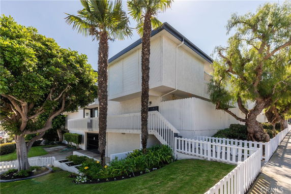 Front view of a multi-story house with white fencing and surrounding greenery.