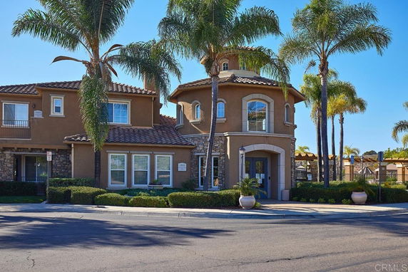 Front view of a multi-story building with a tiled roof and palm trees.