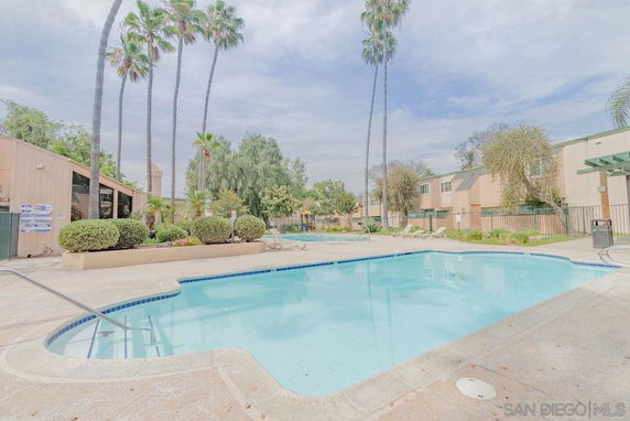 Outdoor swimming pool with surrounding residential buildings and palm trees.
