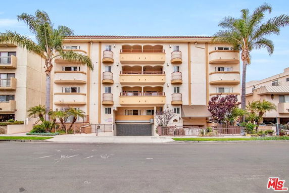 Front view of a multi-story residential building with balconies and palm trees.