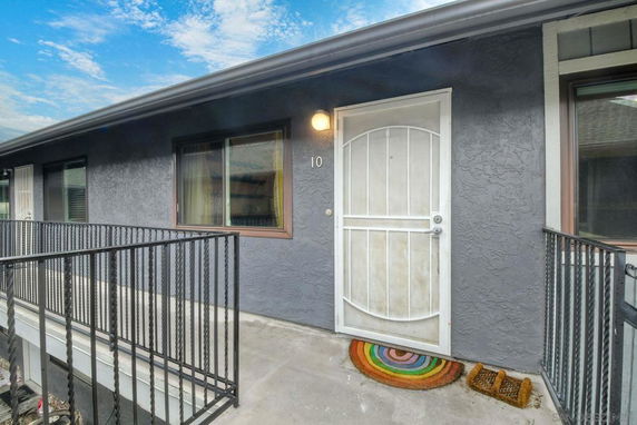Exterior walkway with metal railing leading to a door marked number 10 of a building.