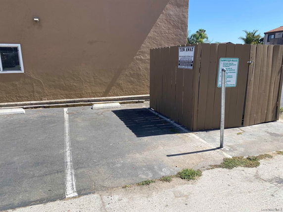 Outdoor parking area with designated parking spaces and a fenced-off dumpster area.