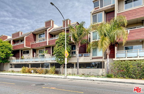 Front view of a multi-story residential building with balconies and palm trees in front.