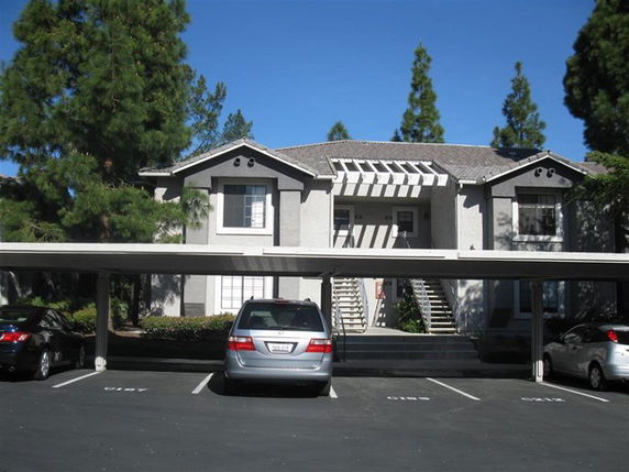 Outdoor parking area with covered parking spaces in front of a residential building.