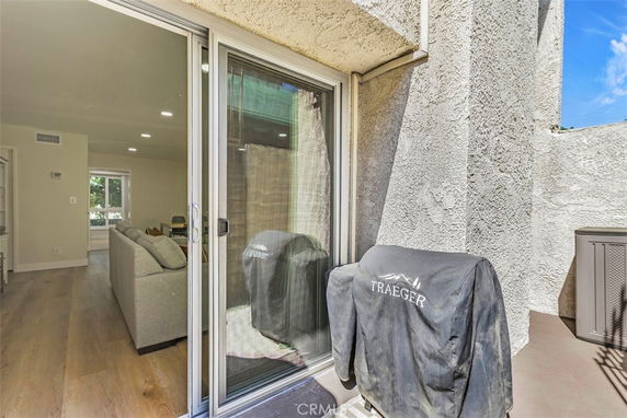 View from a patio with a grill next to a sliding glass door leading to a living area inside.