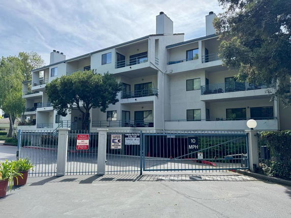 Front view of a three-story apartment building with balconies and gated entrance.
