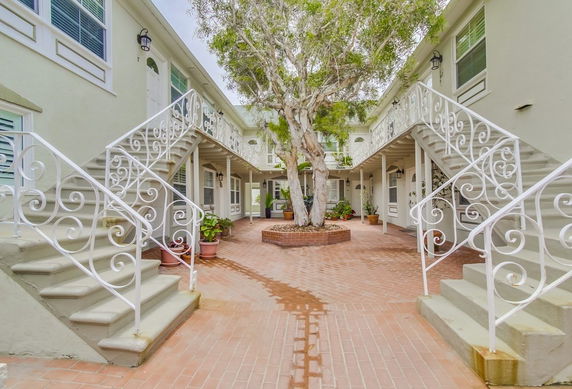 Courtyard view of an apartment complex with symmetrical stairs and a central tree.