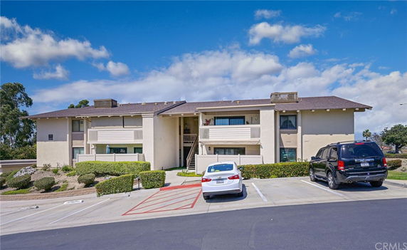 Front view of a two-story residential building with balconies and parking area in front.