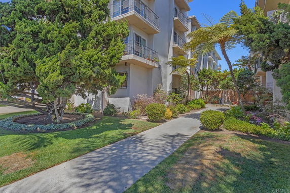 Front view of a multi-story residential building with balconies and a landscaped walkway.