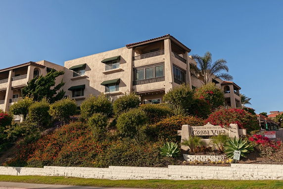 Front view of a multi-story building with balconies and a garden in the foreground.