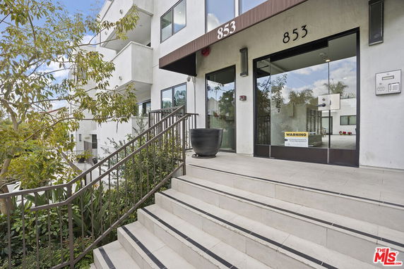 Front view of a multi-story building entrance with stairs and glass doors.