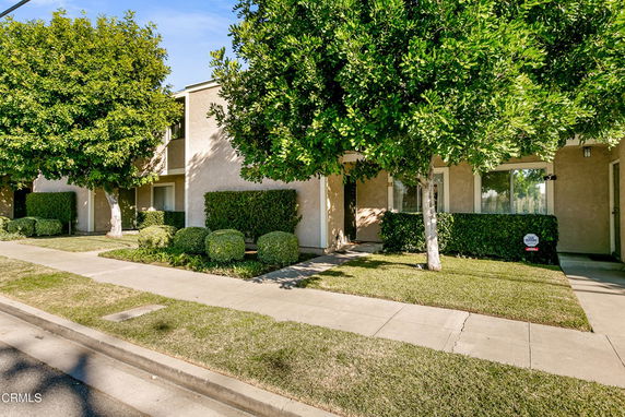 Front view of a residential building with a beige exterior and greenery.