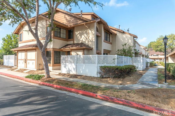 Front view of a multi-story residential building with a white fence and brown accents.
