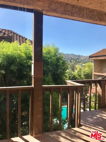 View from a balcony showing surrounding greenery and rooftops.