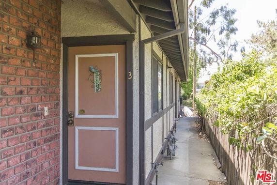 Front view of a building entrance with a brown door and brick wall.