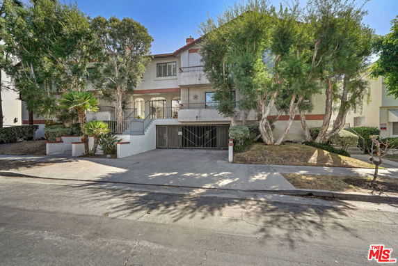 Front view of a multi-story residential building with gated entry and trees at the front.