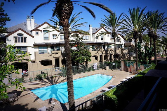 Outdoor swimming pool area with palm trees in front of a multi-story residential building.